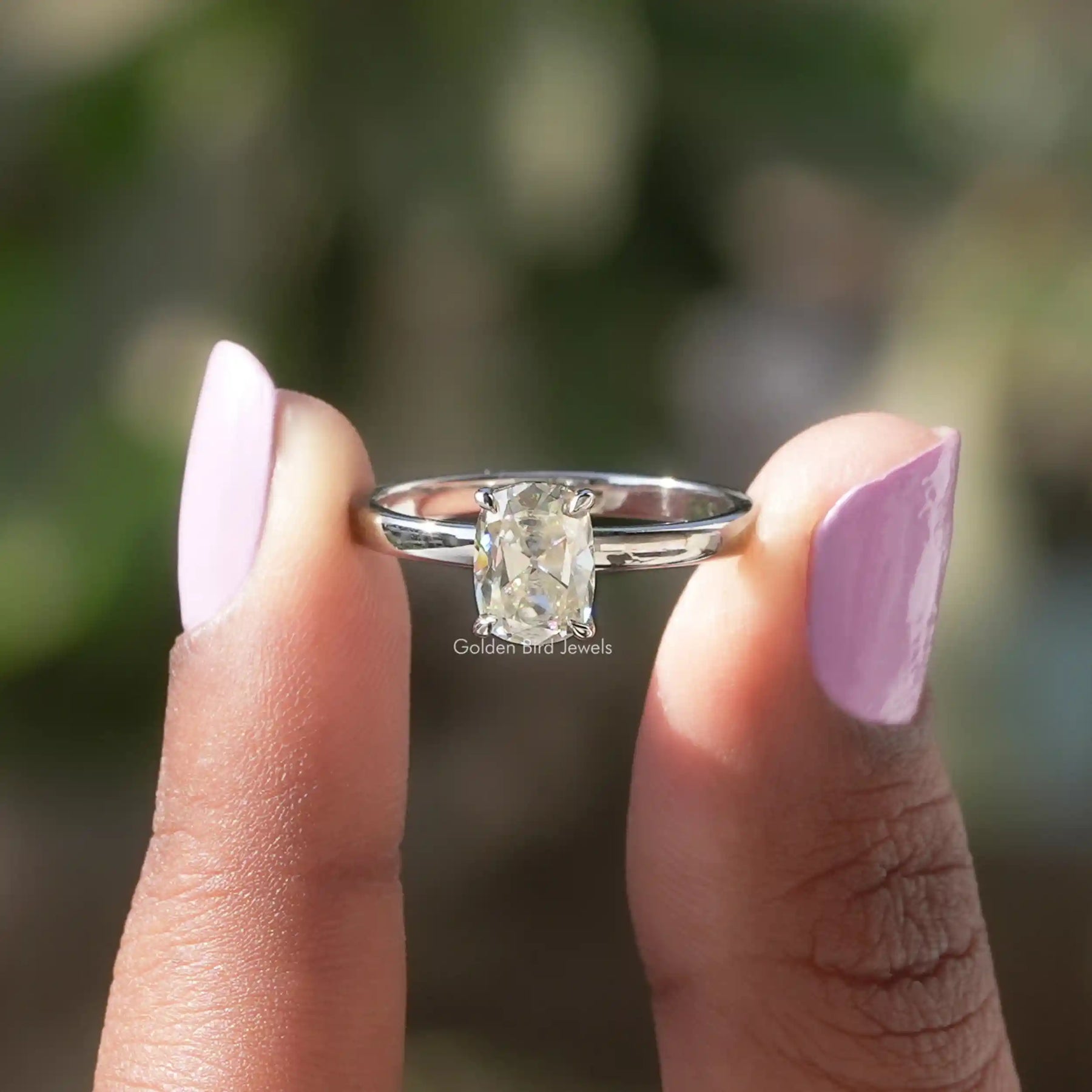 Two fingers holding the 1 Carat Cushion Cut Moissanite Ring