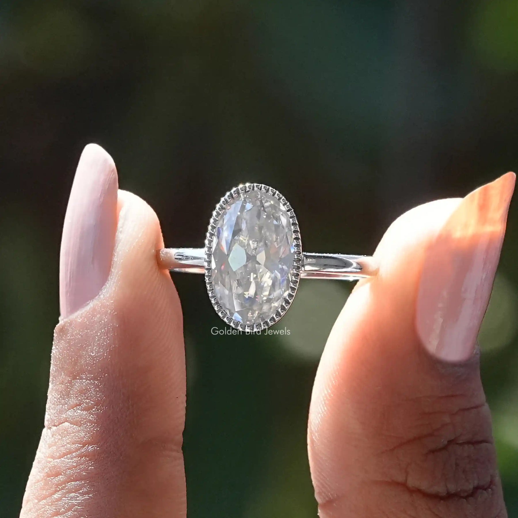 Two fingers holding the Oval Cut Bezel Set Moissanite Engagement Ring