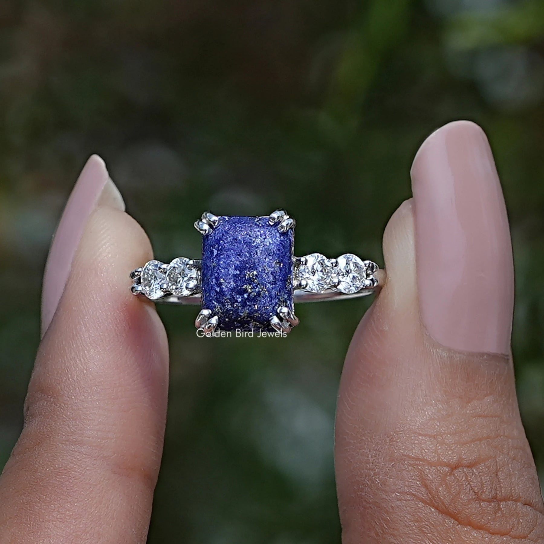 Two fingers holding the Blue Emerald Cut Gemstone Engagement Ring