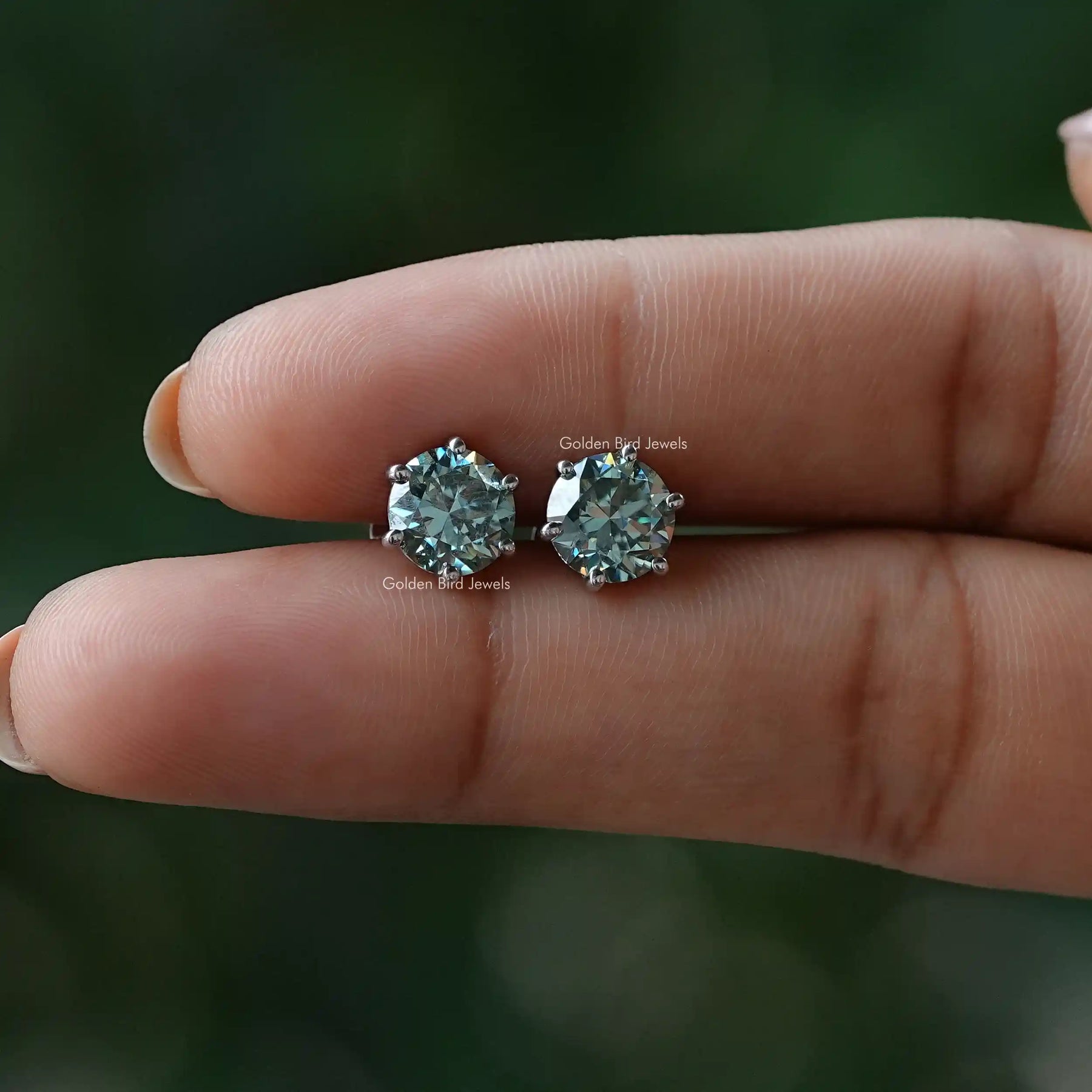 In finger view of blue round cut stud earrings
