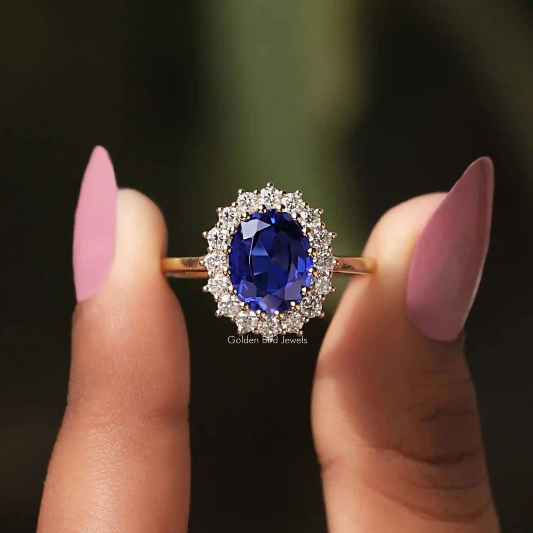 Front View Of Sapphire Blue Oval Cut Halo Engagement Ring In a Two Fingers