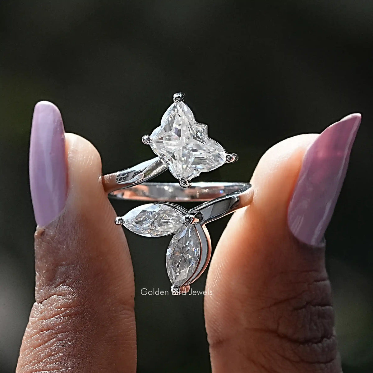 Two fingers holding the Colorless Butterfly Cut Moissanite Bypass Ring