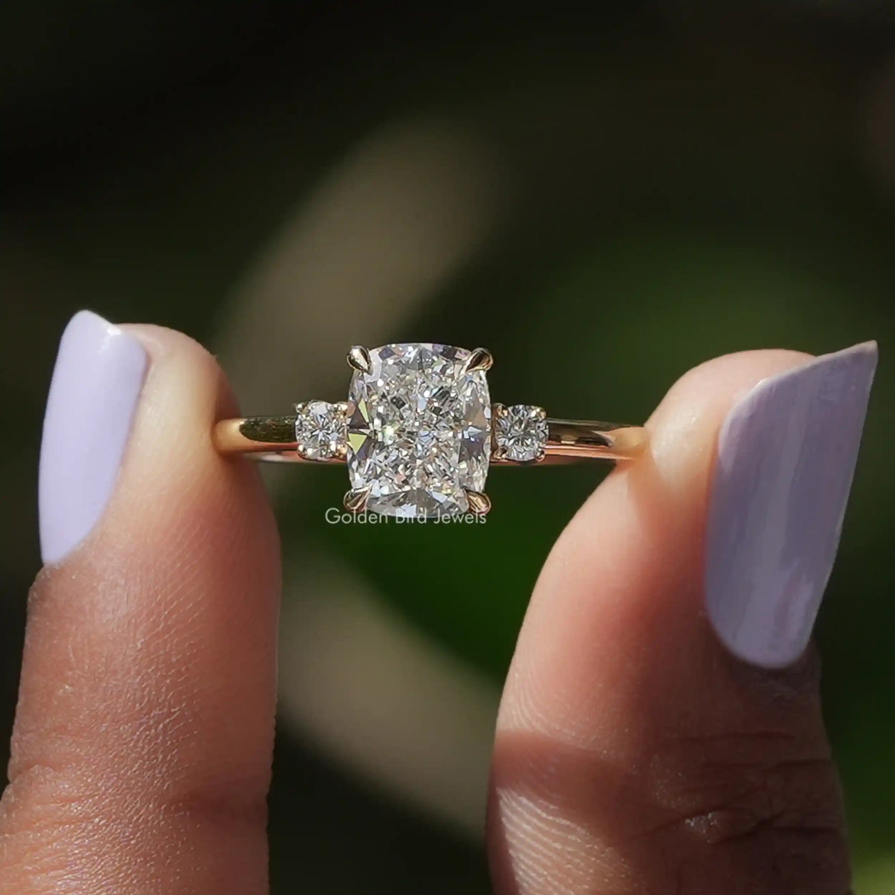 Cushion Cut Diamond Three Stone Ring held between two fingers