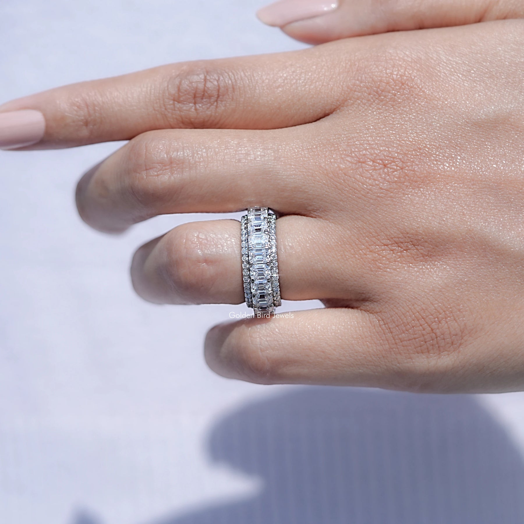 In finger front view of Emerald and Round Cut moissanite three row band in unique shape