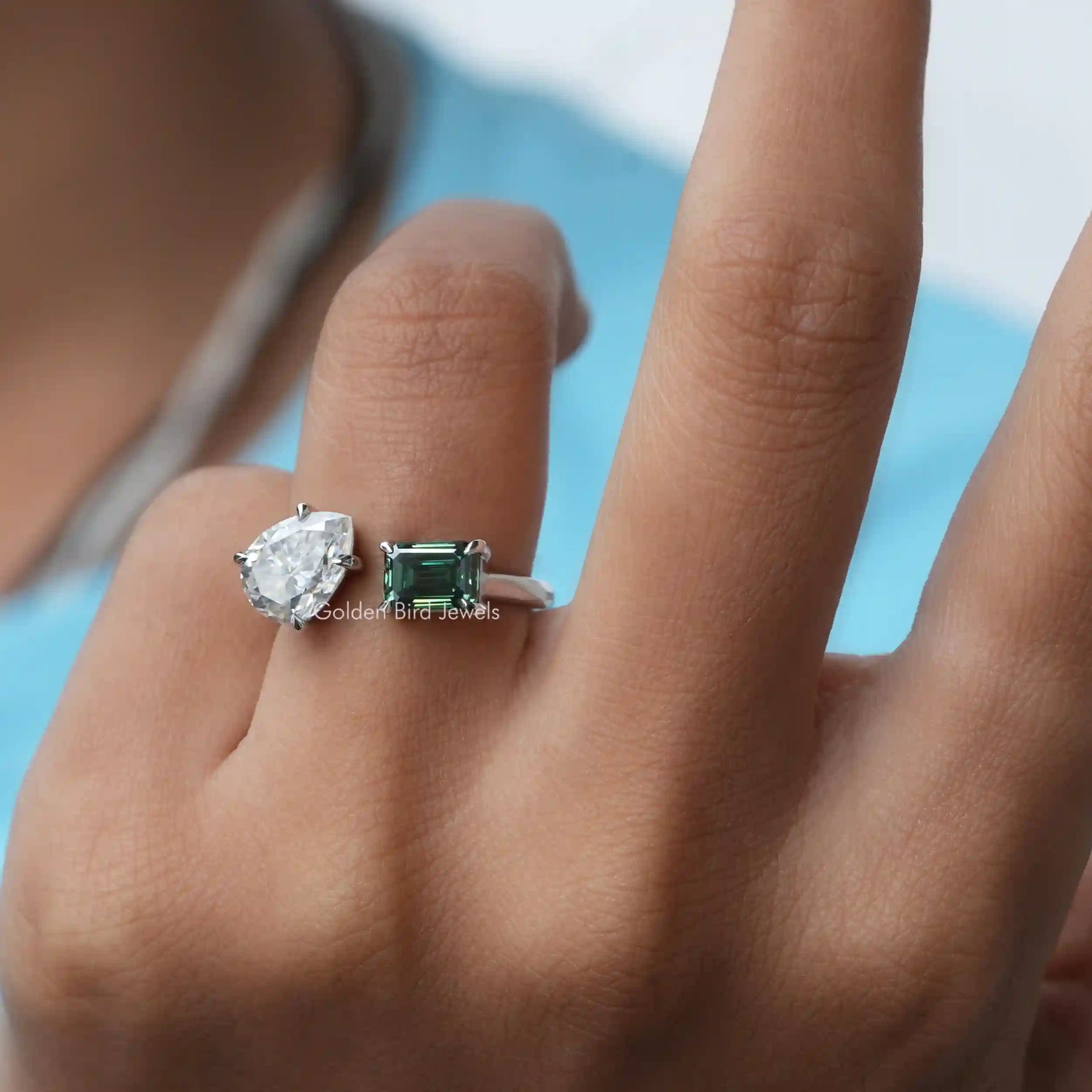 In finger front view of an emerald cut and pear-shaped Moissanite ring