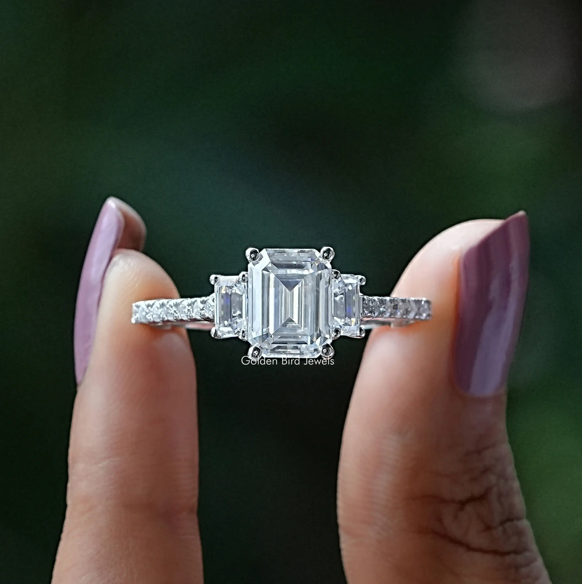 Front View of Emerald Cut Three Stone Moissanite Engagement Ring In two Fingers