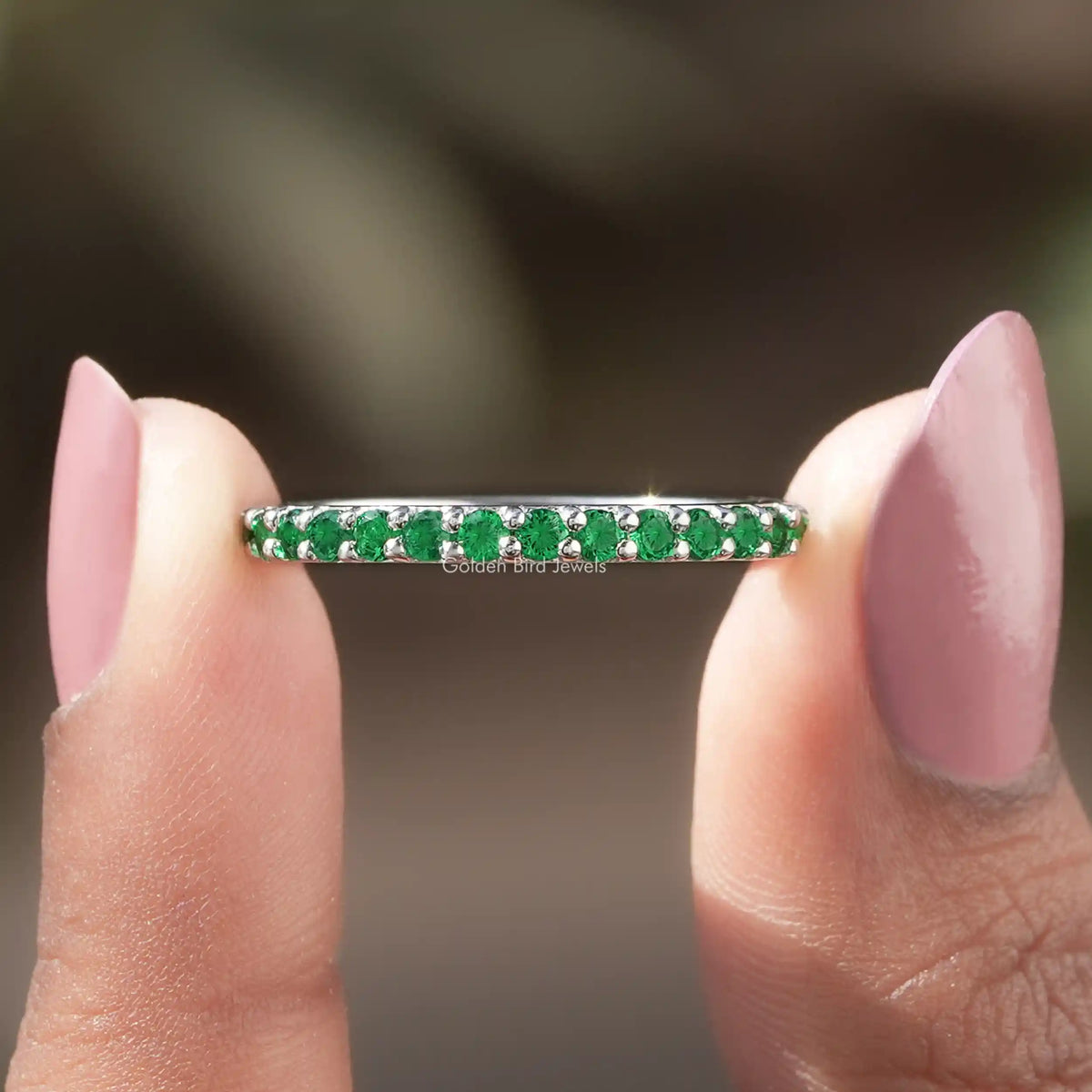 Green gemstone ring held between two fingers with a blurred background