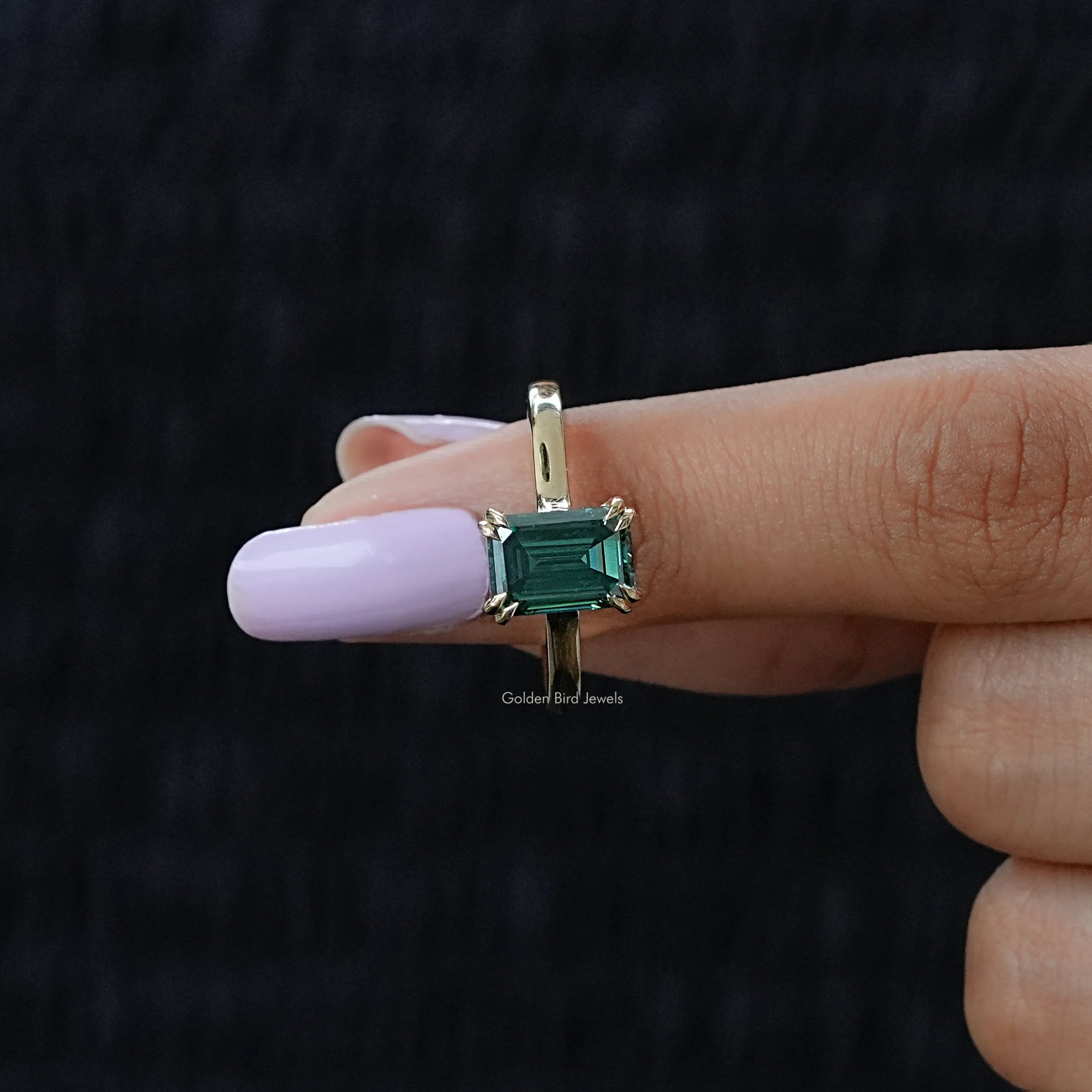 In finger front view of Green emerald moissanite ring in secure setting