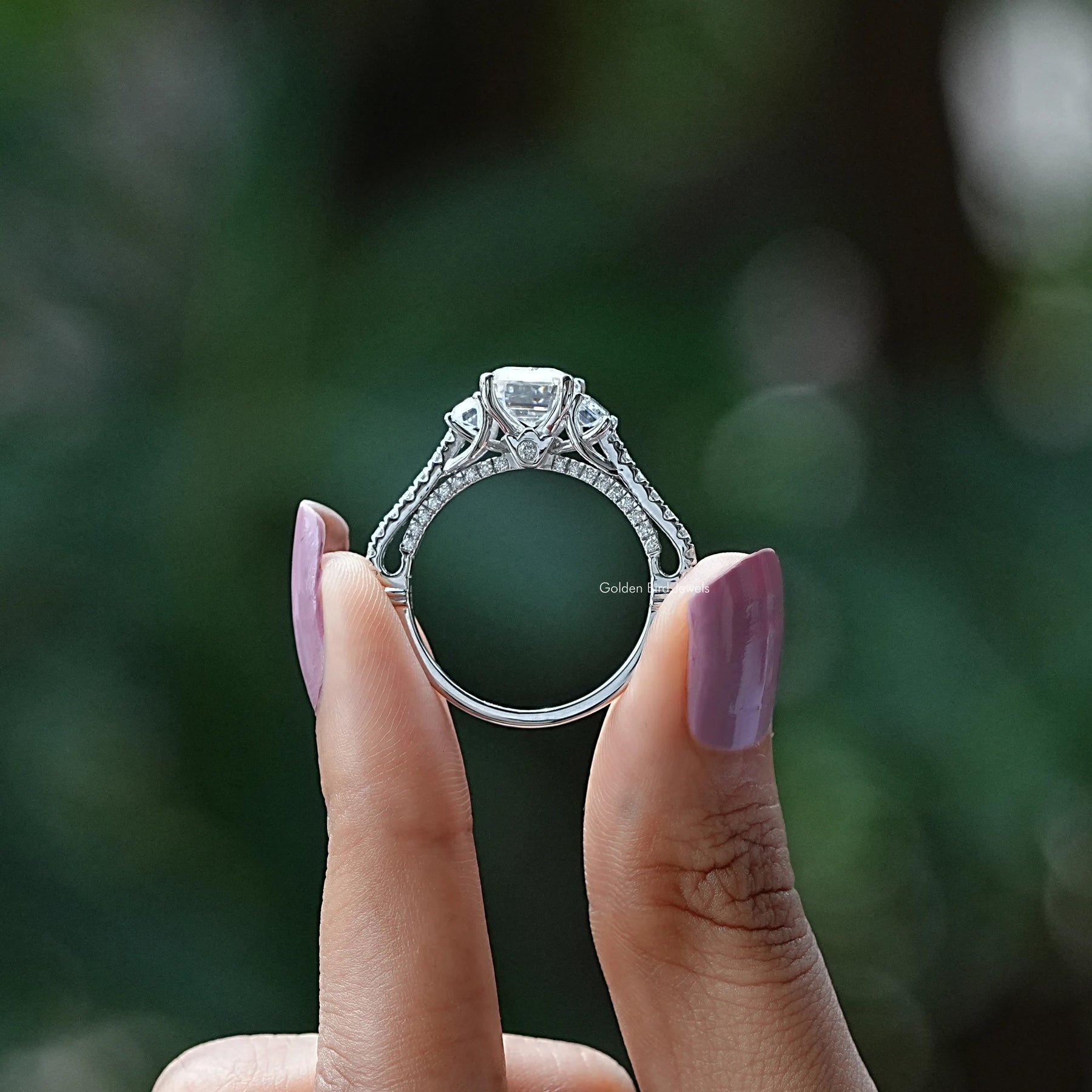 Back View of Emerald Three Stone Moissanite Engagement Ring In two fingers