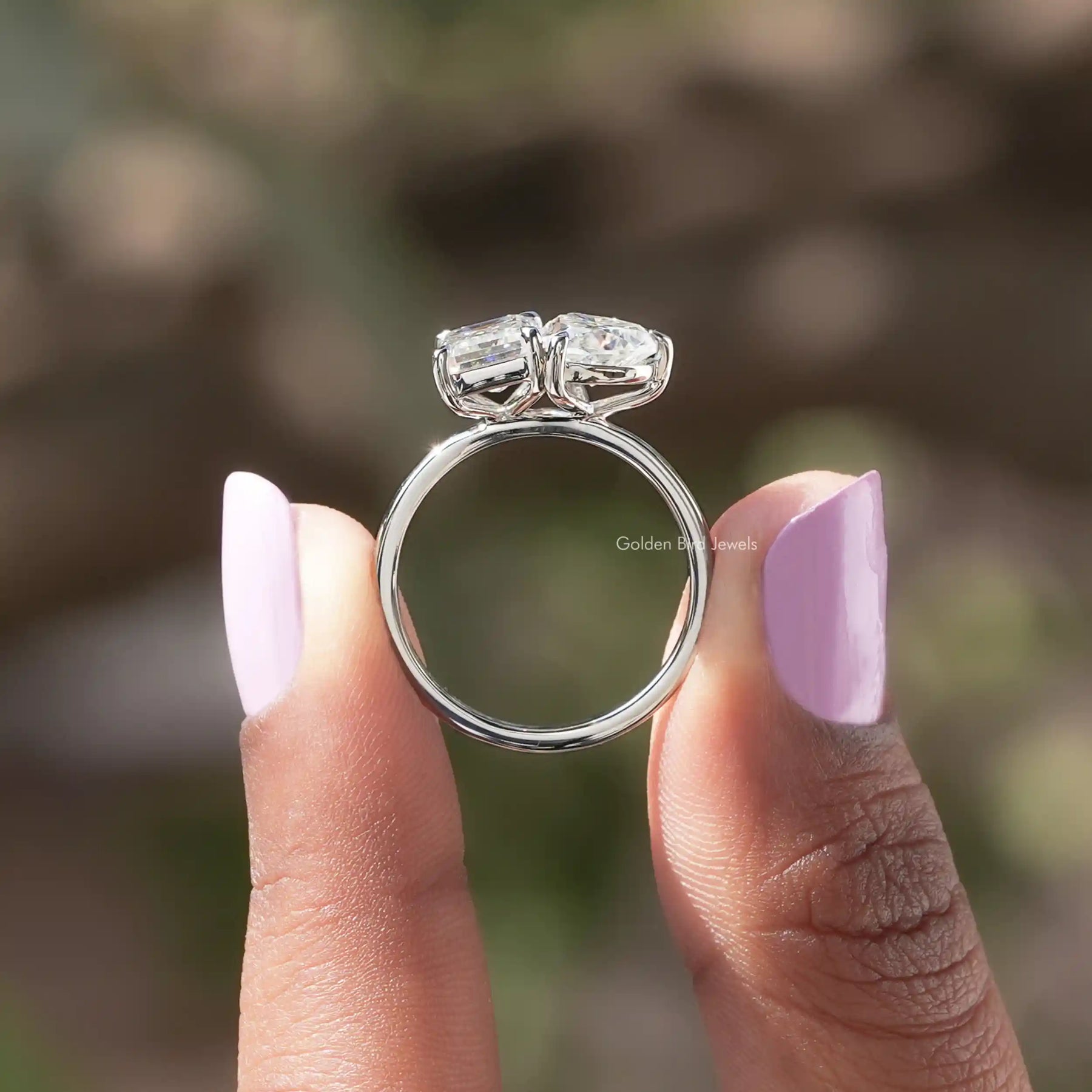 Back view of heart and emerald cut moissanite ring holding on two fingers