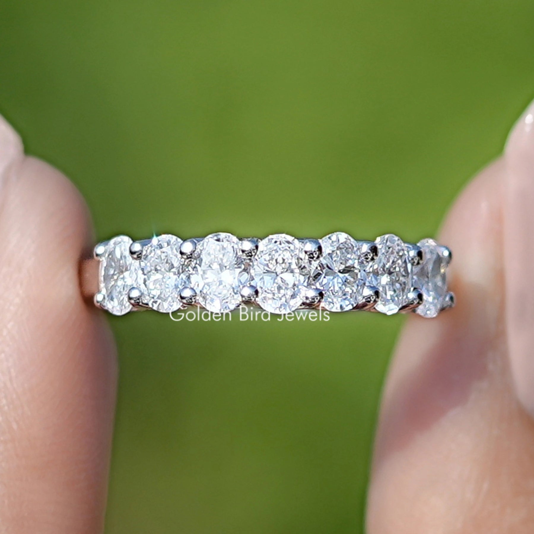 Lab Grown Diamond Oval Seven Stone Wedding Band Held Between Fingers