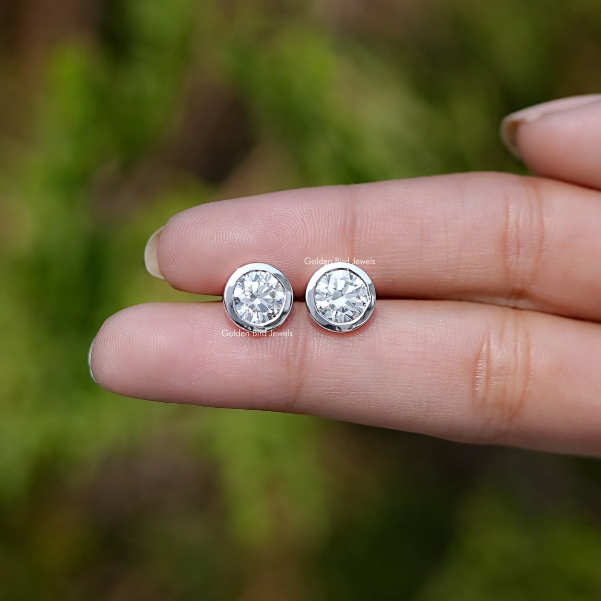 Front View of Diamond Round Cut Bezel Set Stud Earrings In Fingers