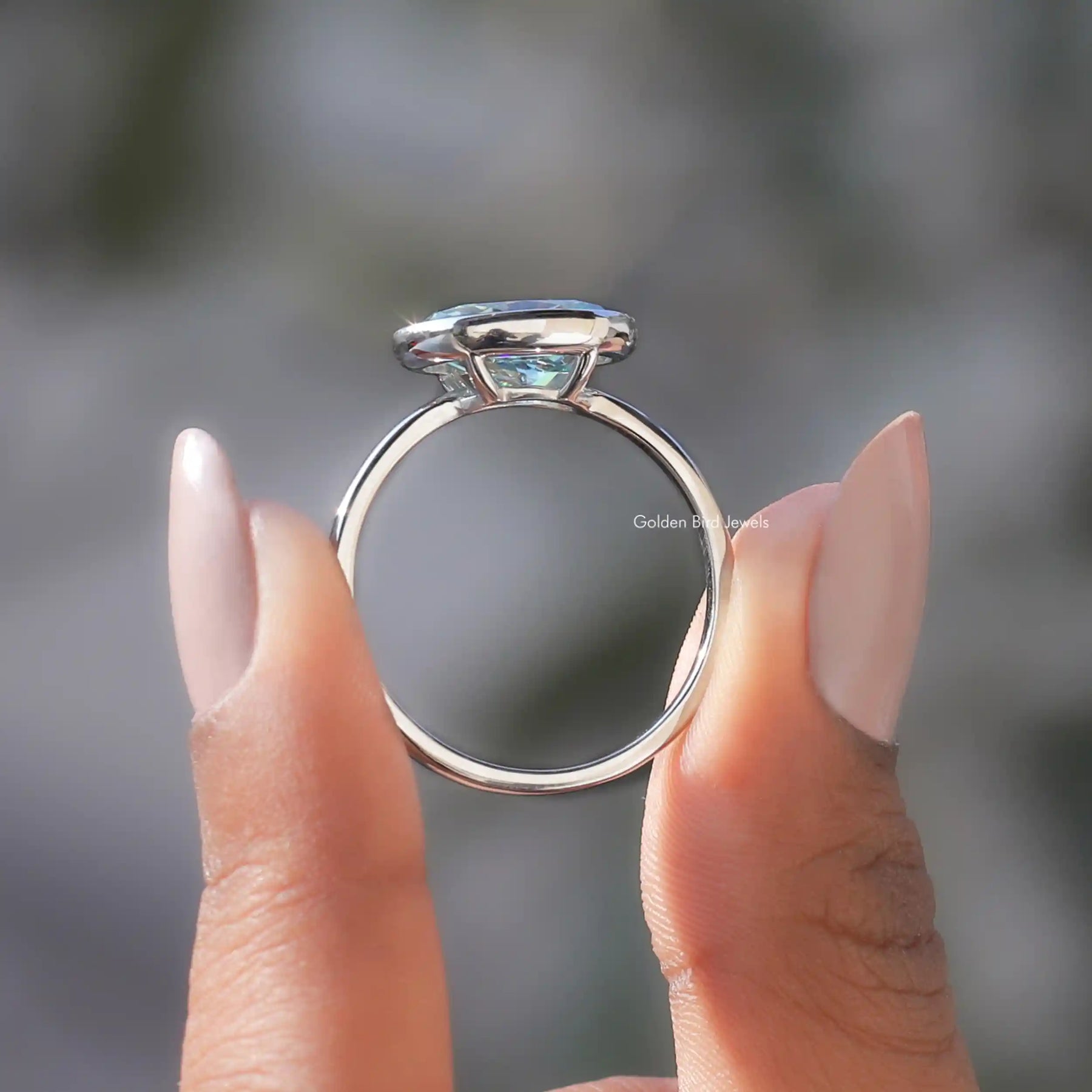 Back View of Blue Oval Cut Moissanite Bezel Set Ring In two fingers