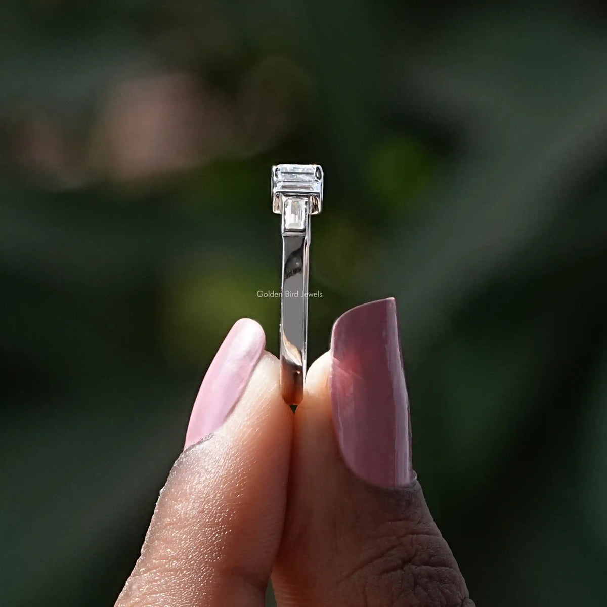 Side View of Colorless Emerald And Baguette Cut Moissanite Ring In two fingers