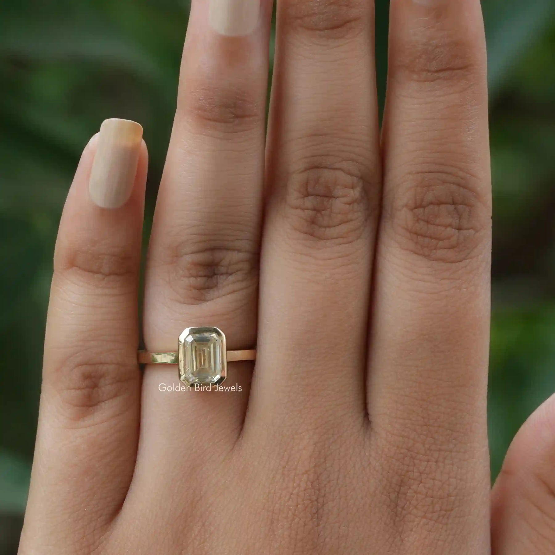 Bezel set emerald cut solitaire moissanite ring on finger.