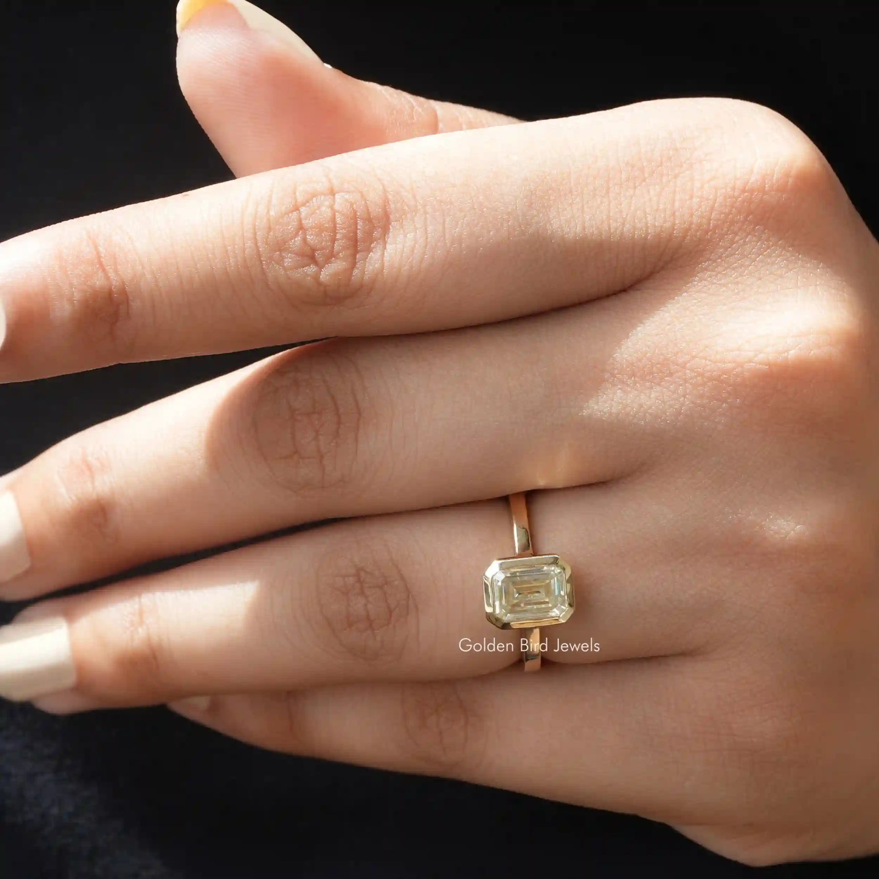 Classic emerald cut solitaire moissanite engagement ring shown on hand.