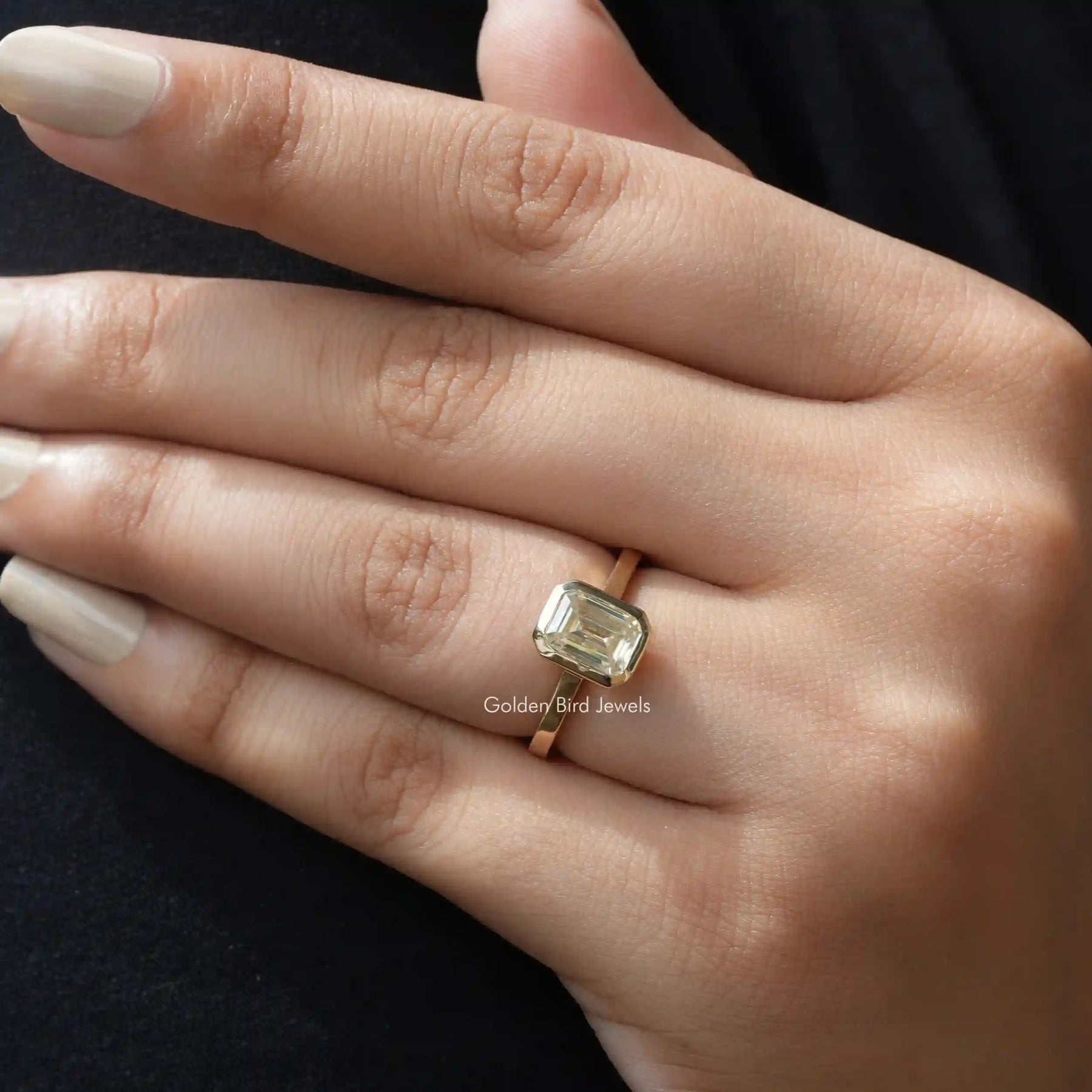 Front view of emerald cut solitaire moissanite ring on finger.