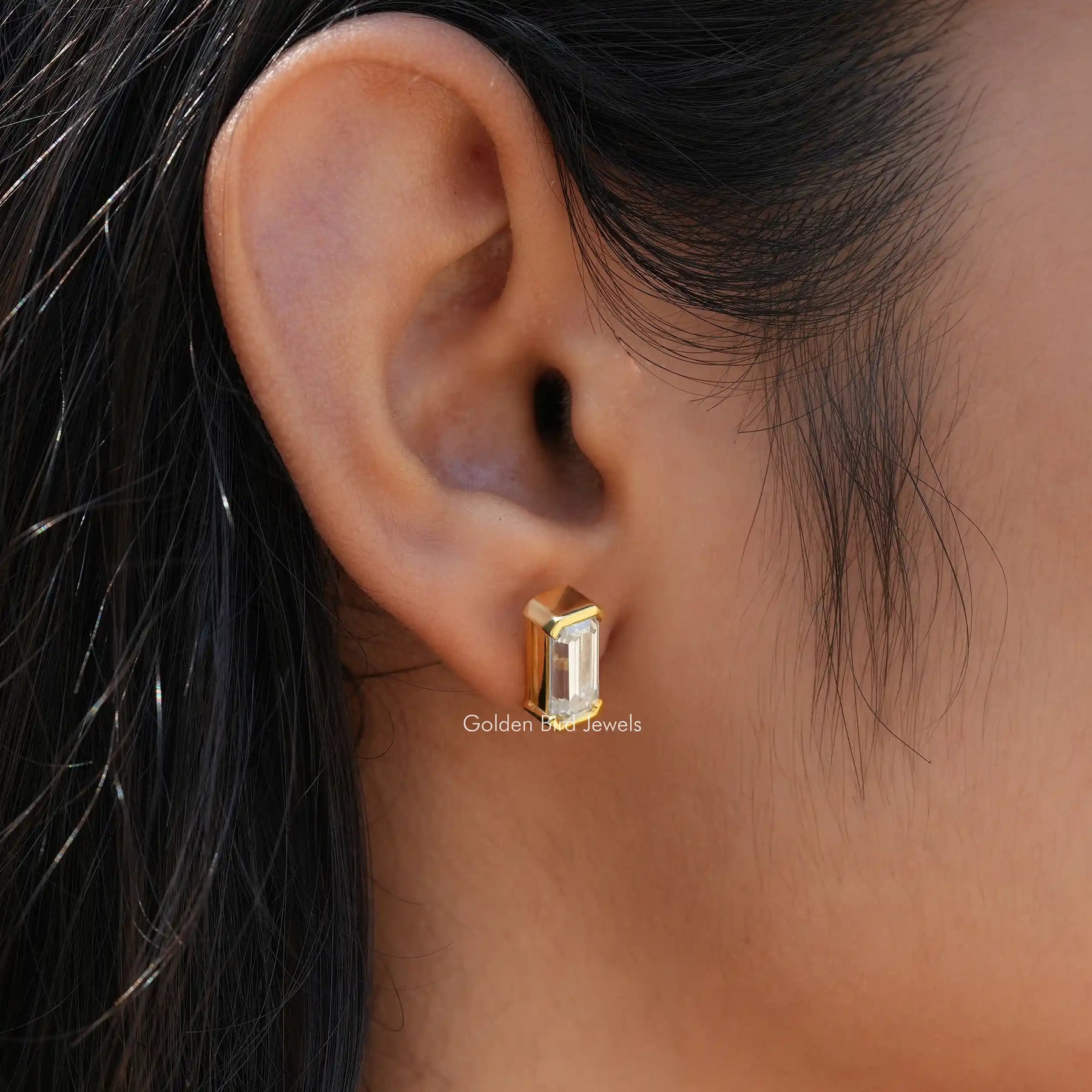 In ear front view of bezel set emerald cut earrings in yellow gold