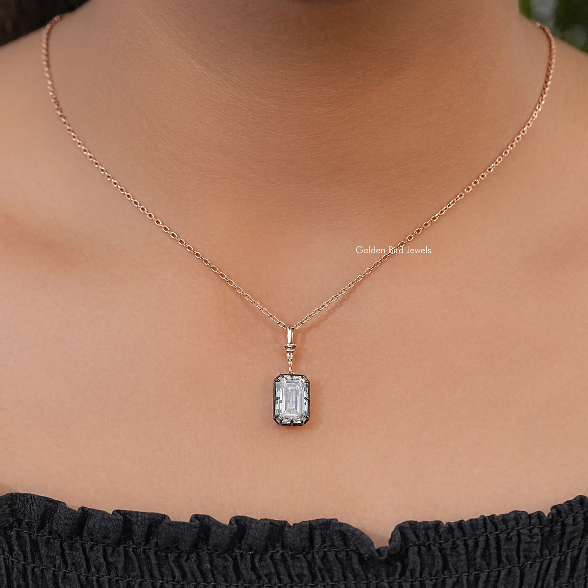 Solitaire pendant necklace worn on a fine chain, with a clear emerald-cut stone and dark setting
