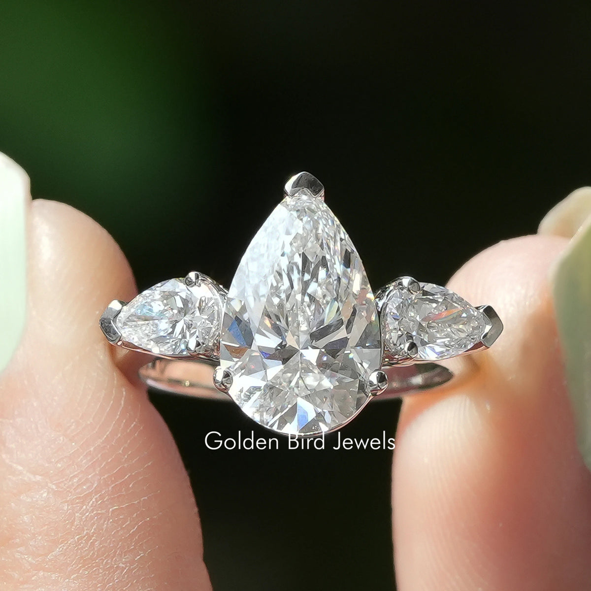 Three Stone Pear Shaped Diamond Engagement Ring Held Between Fingers