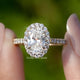 Oval Cut Lab Diamond Halo Engagement Ring Held Between Fingers