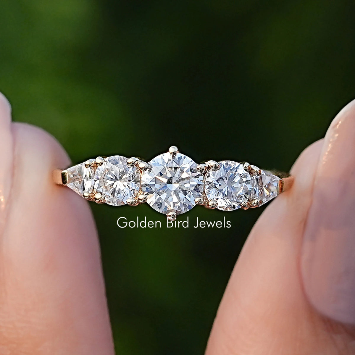 Shield And Round Cut Lab Diamond Five Stone Ring Held Between Fingers