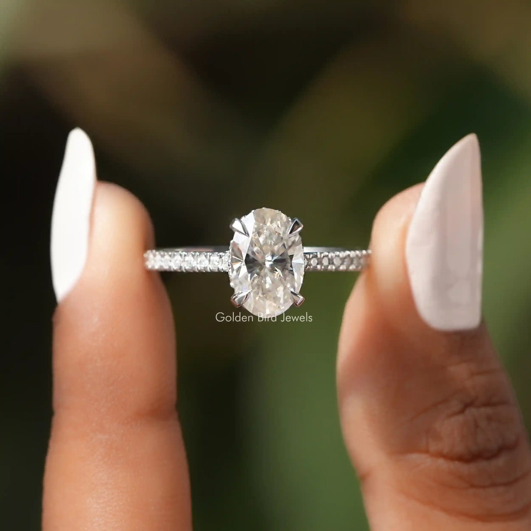 Two fingers holding the Moissanite Oval Cut Hidden Halo Accent Stone Ring
