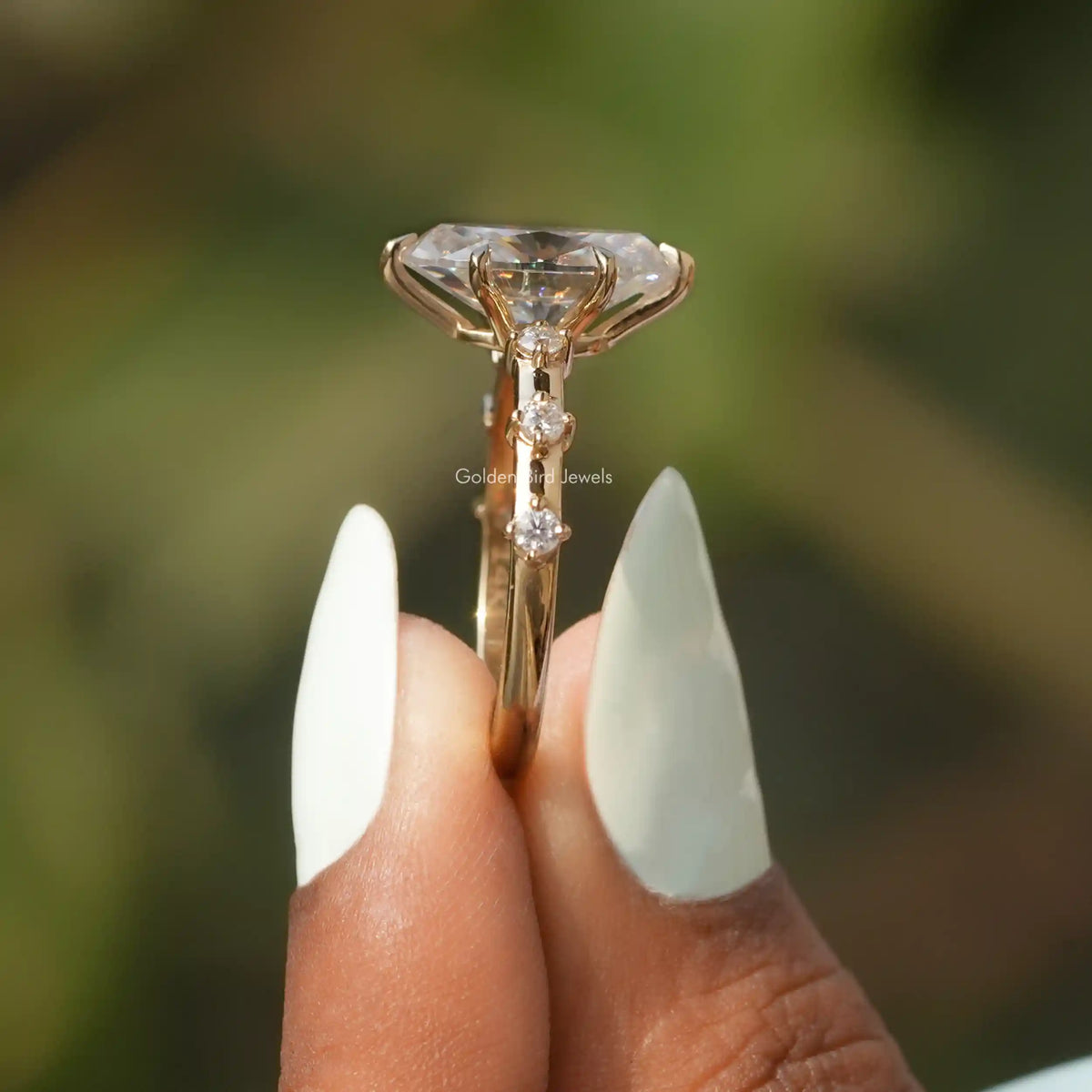 Side View of Oval Cut Accent Stone Engagement Ring In two fingers