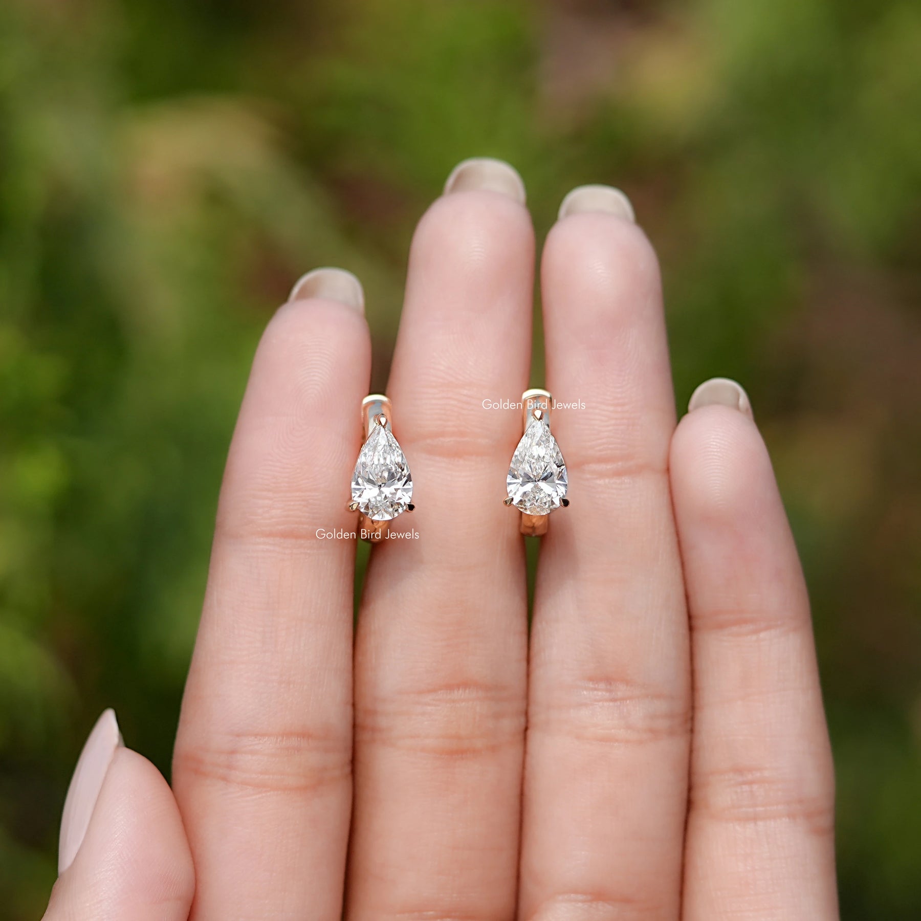 Front View of Pear Cut Solitaire Huggie Hoop Earrings In Fingers