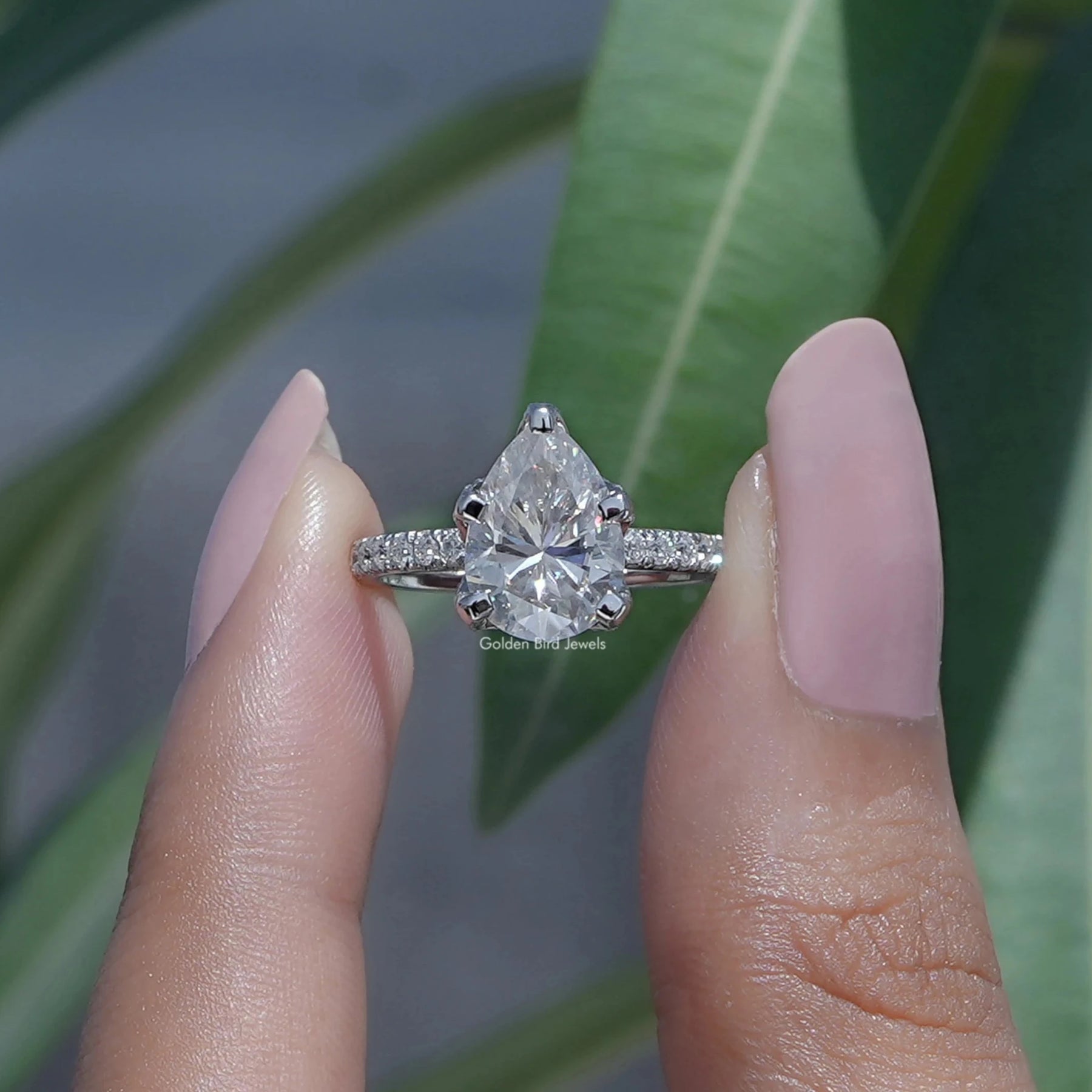 Two fingers holding the Pear Shaped Moissanite Accent Stone Ring