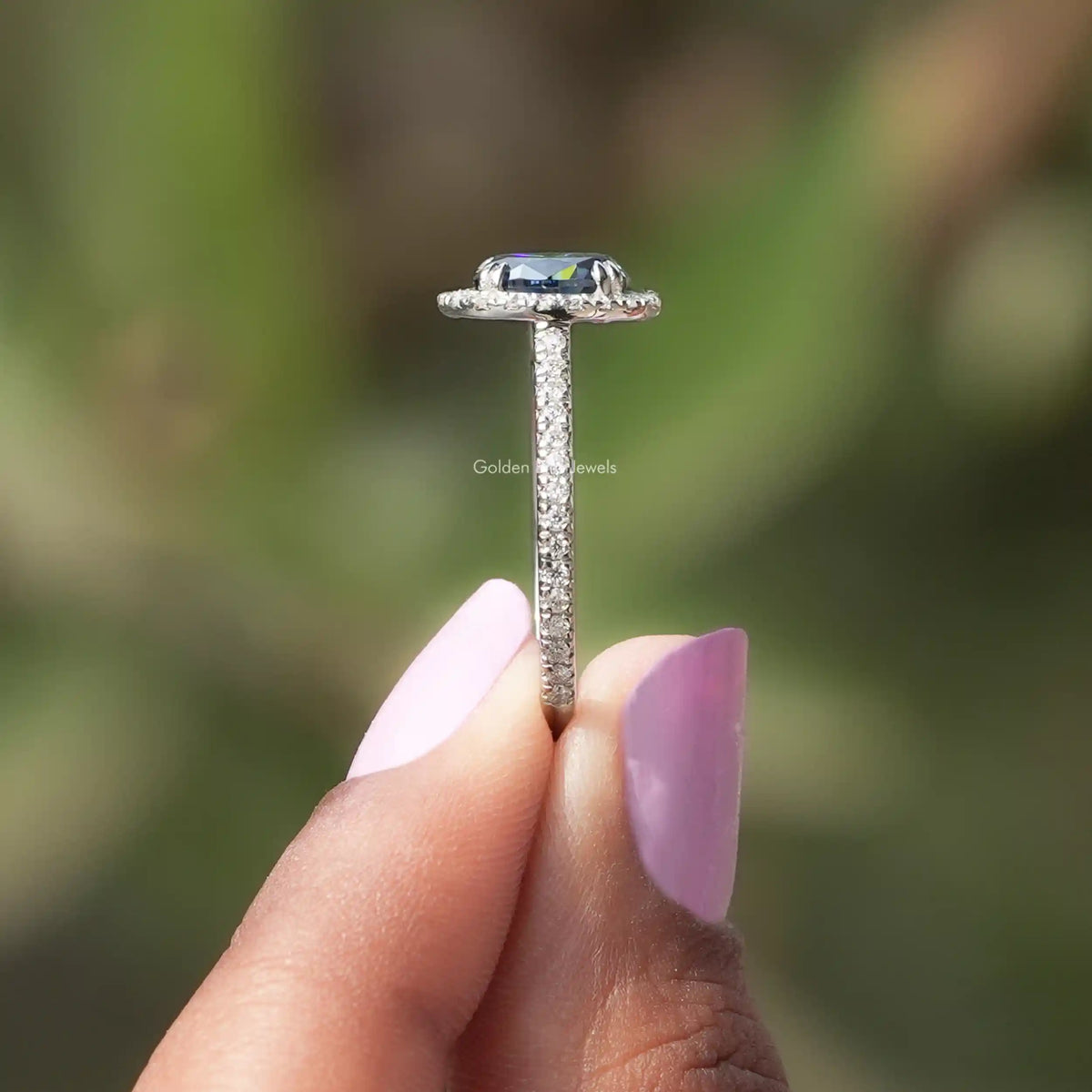 Side View of Blue Oval Cut Accent Stone Engagement Ring In two fingers