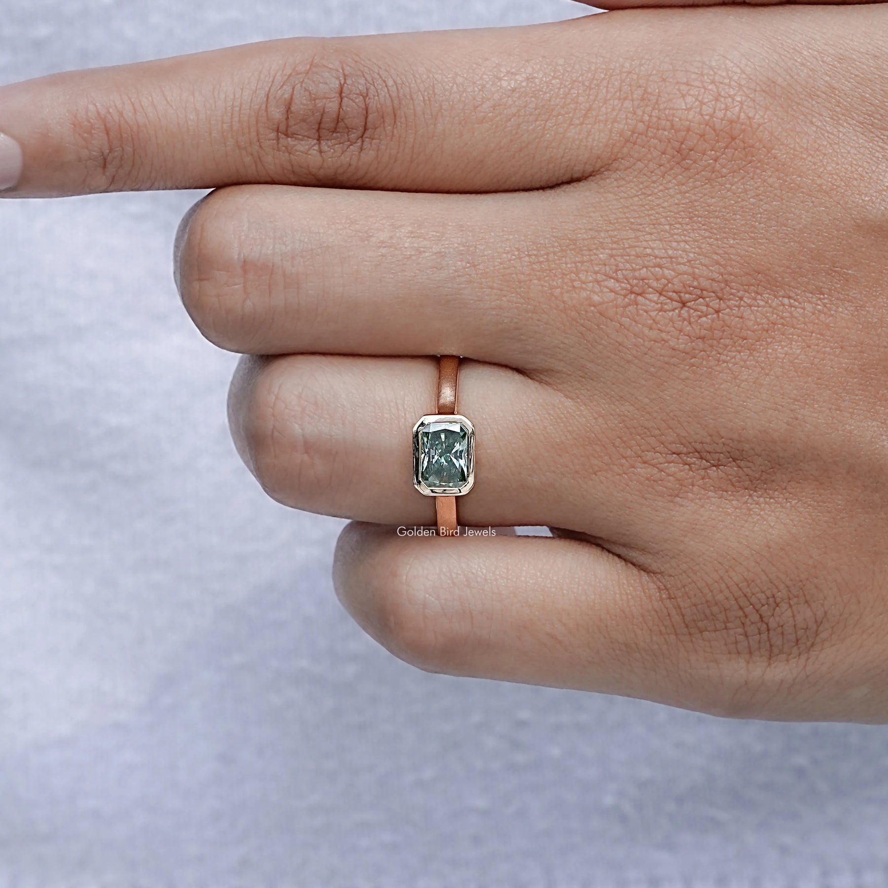 In finger front view of Green Radiant Shape Ring in unique shape