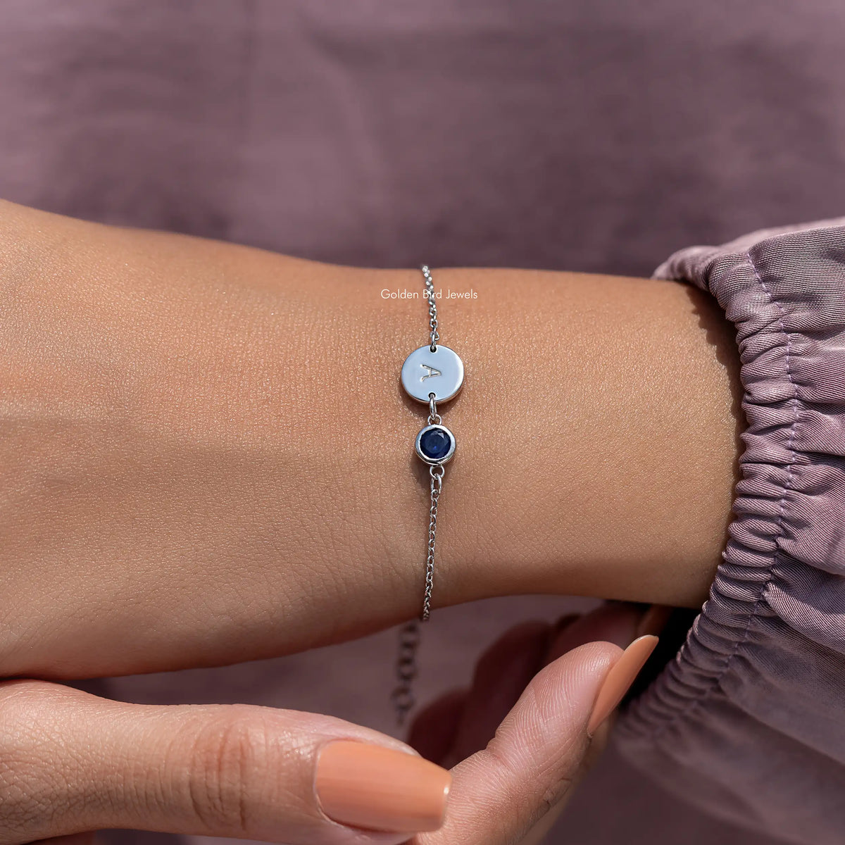 Sterling silver bracelet with letter A disc and blue round gemstone on wrist