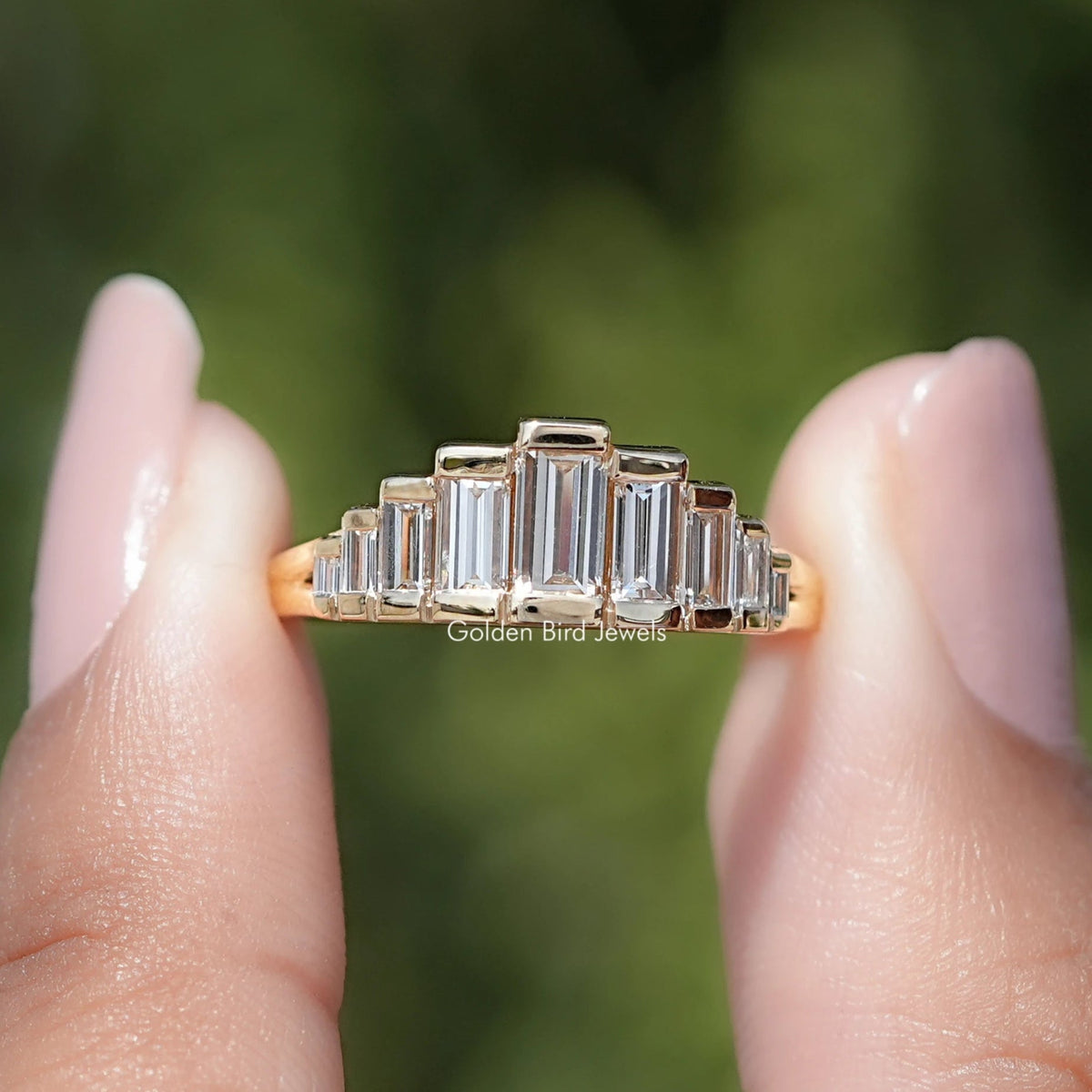 Gold ring with emerald-cut diamonds on a blurred green background