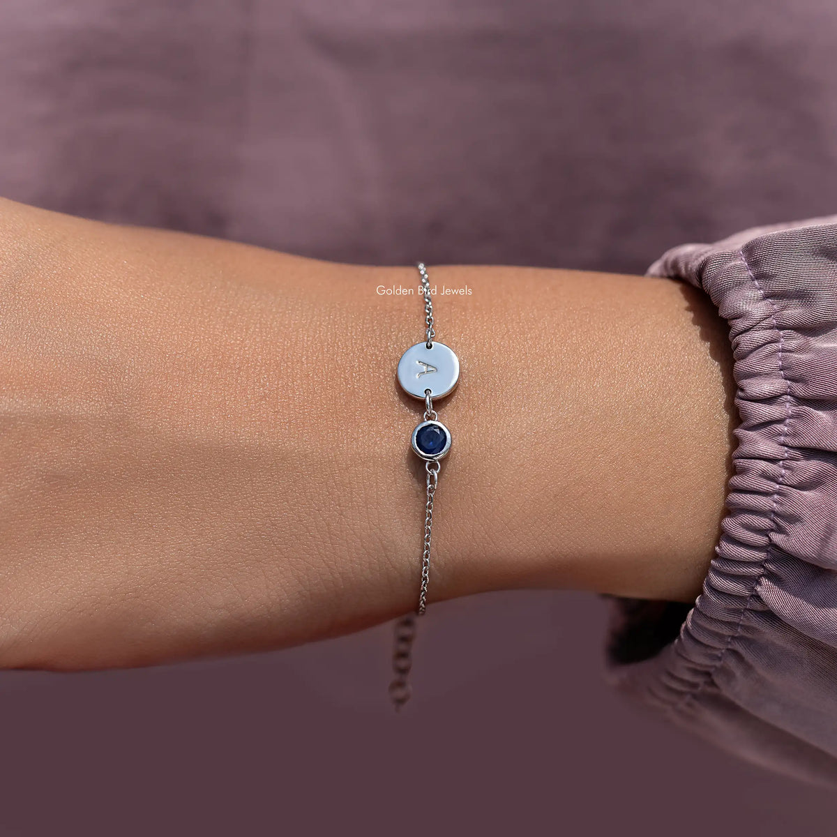 Sterling silver bracelet with letter A disc and blue round gemstone on wrist