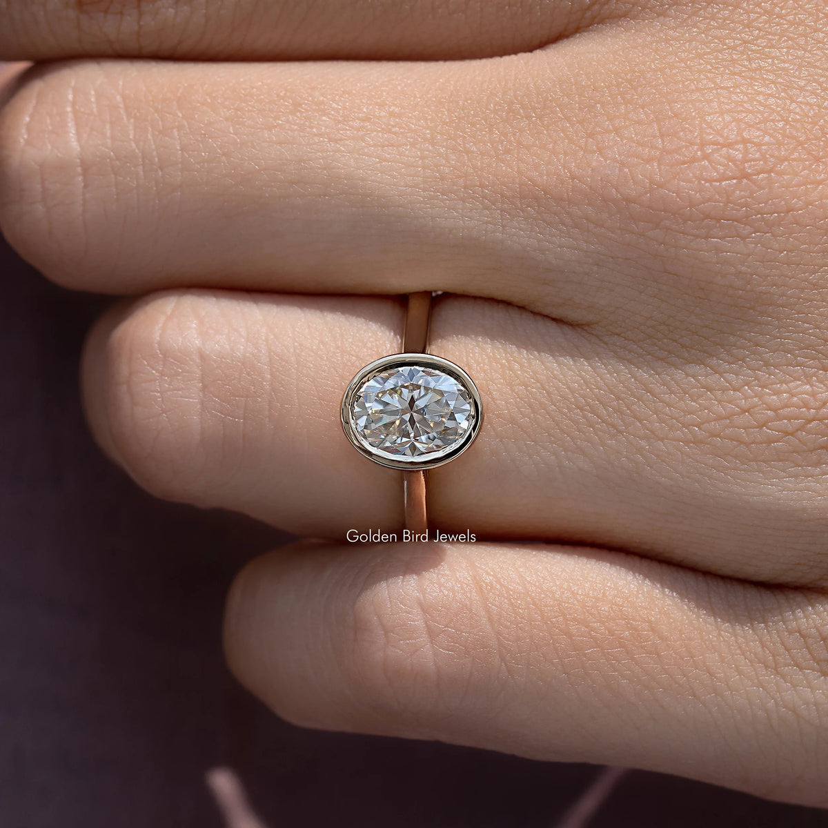 Bezel-set oval moissanite solitaire ring close-up with slim gold band