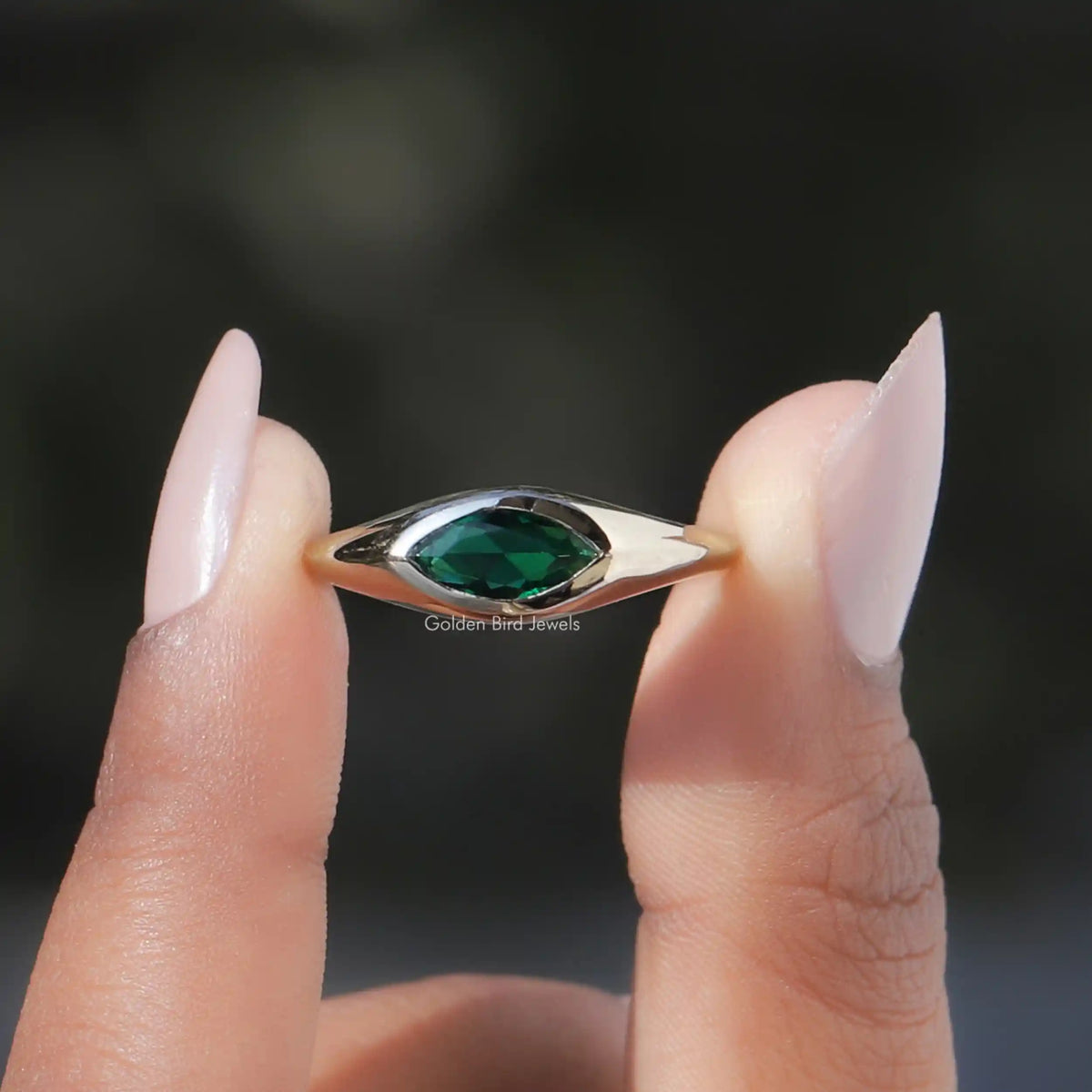 Two fingers holding the Green Marquise Cut Bezel Set Moissanite Ring