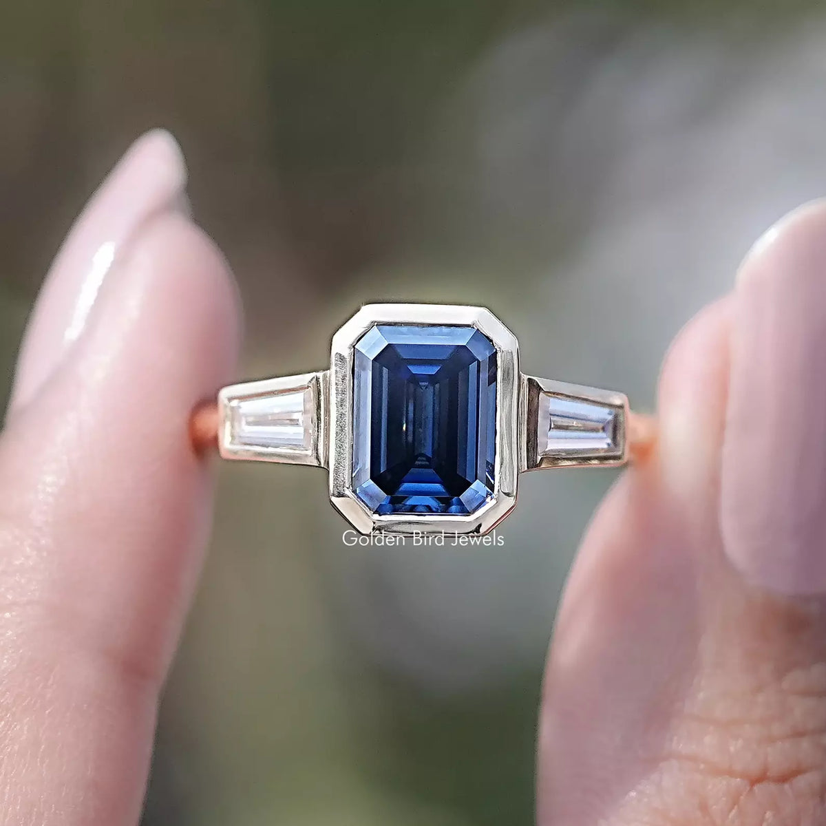 Front view of Blue Emerald Cut Moissanite Three Stone Ring in two fingers 
