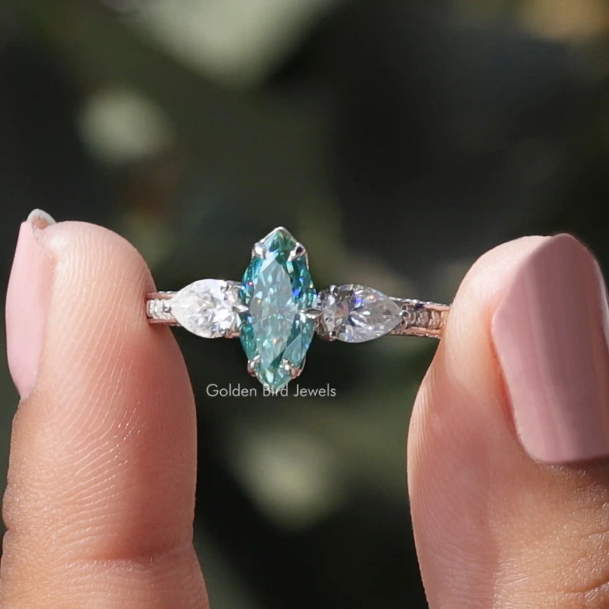 Two fingers holding the Blue Marquise Cut Moissanite Three Stone Ring