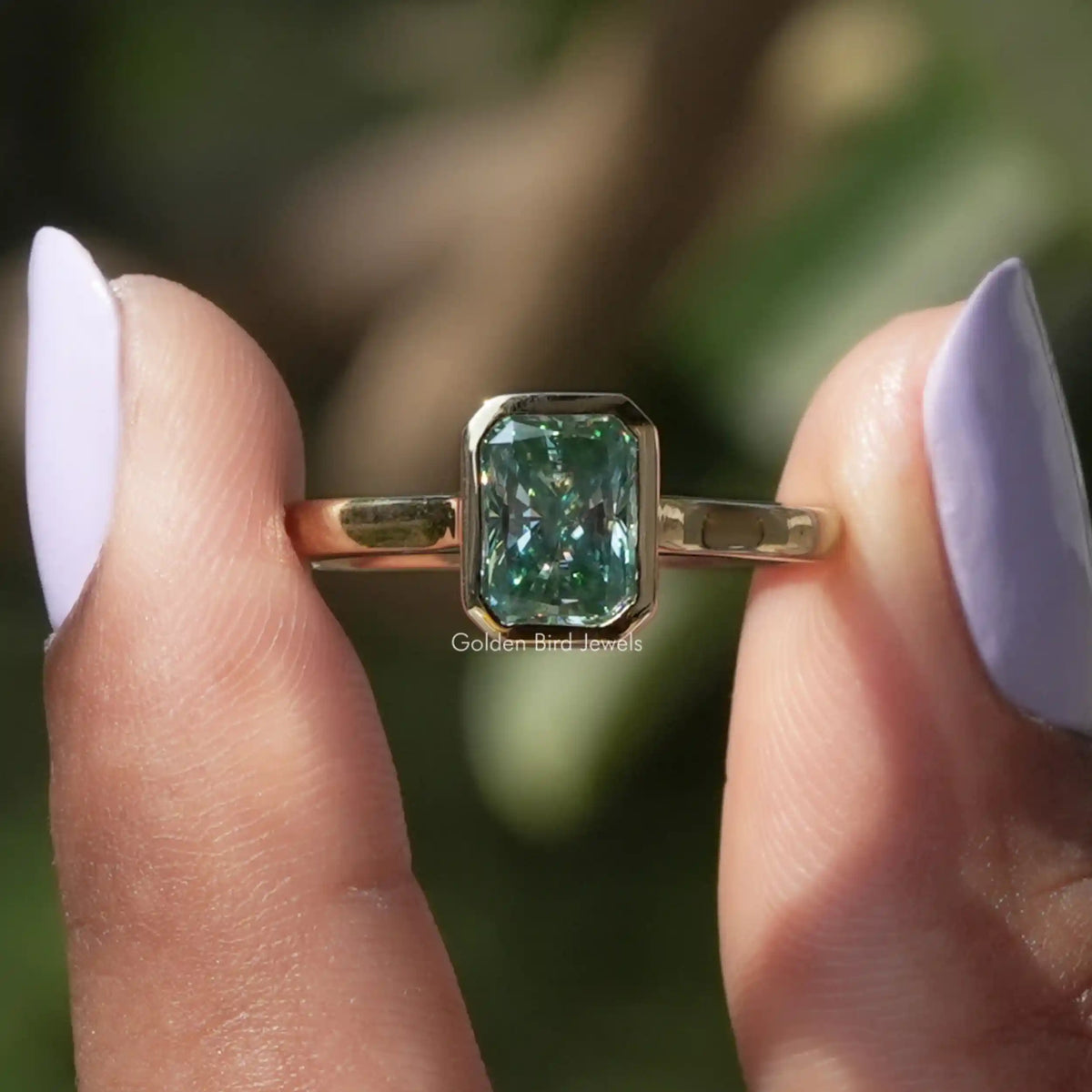 Two fingers holding the Radiant Cut Moissanite Bezel Set Engagement Ring
