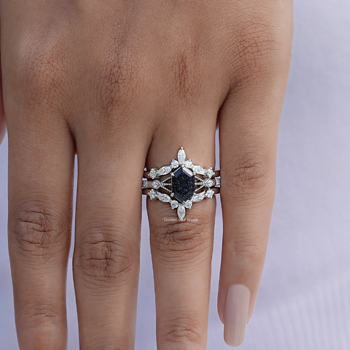 Silver ring on finger with dark blue center surrounded by white marquise and round stones