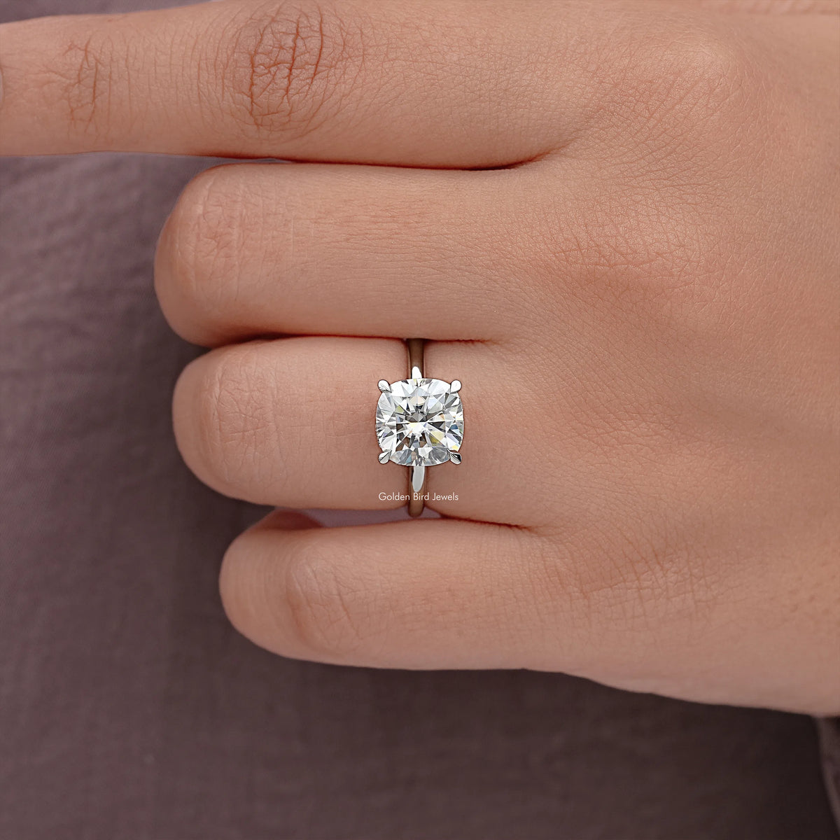 Cushion-cut moissanite solitaire ring on finger with square prongs and silver band