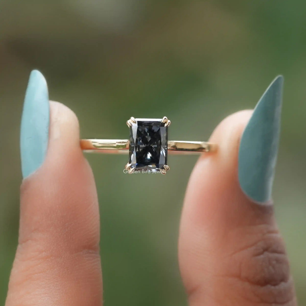 Front view of Dark Gray Radiant Moissanite Solitaire Ring in two fingers 