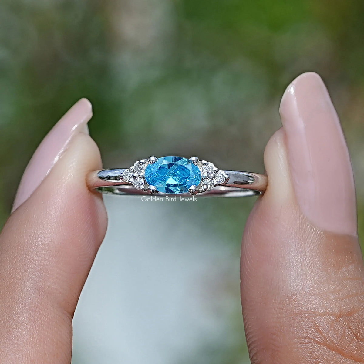 Two fingers holding the East West Aquamarine Oval Cut Ring