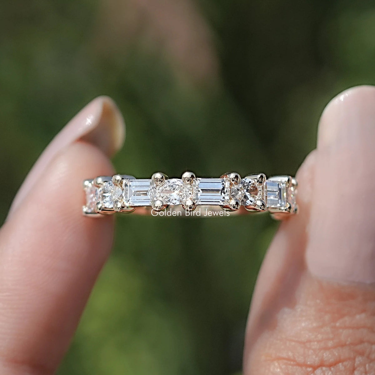 A diamond ring held between two fingers with a blurred green background