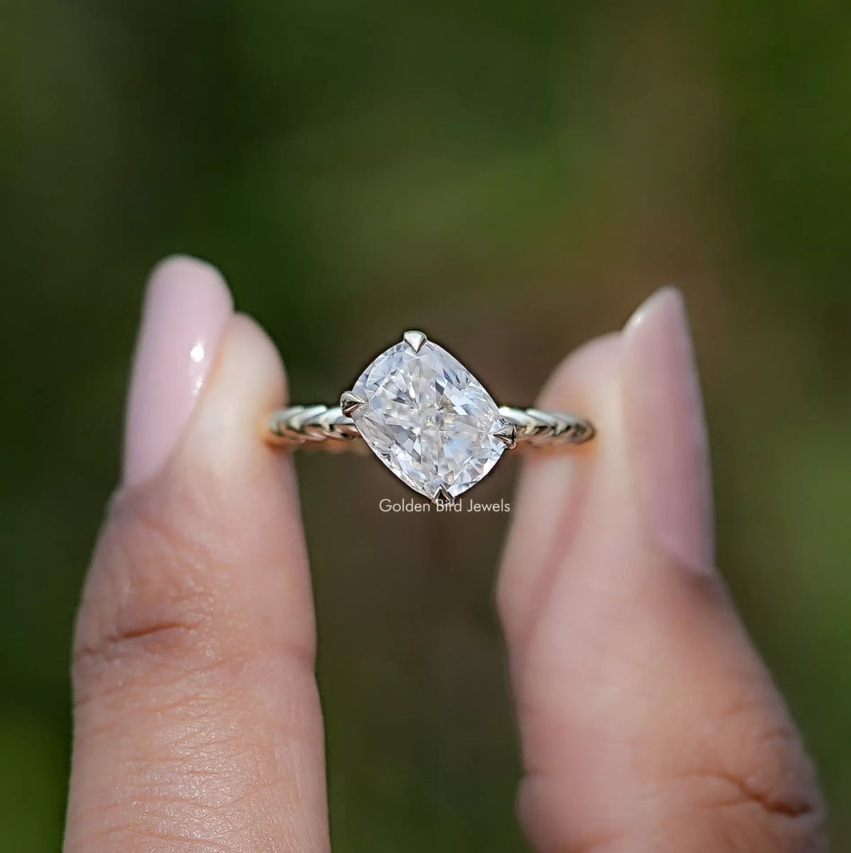 Front view of Cushion Cut moissanite engagement ring holding in two fingers 