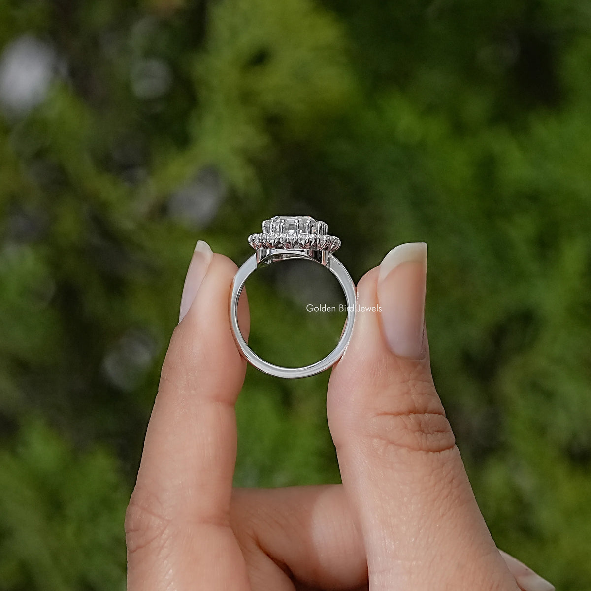Silver ring shown from the side, with a raised emerald-cut center stone and halo setting
