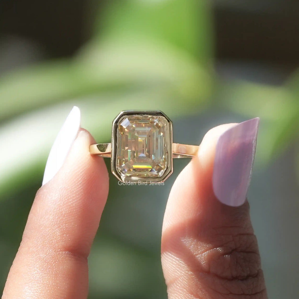 Two fingers holding the Emerald Cut Moissanite Engagement Ring