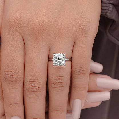 Cushion-cut solitaire engagement ring on finger with silver band and prong-set stone