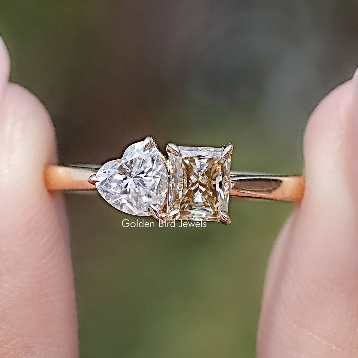 Front view of Radiant And Heart Cut Moissanite Two Stone Ring in two fingers 
